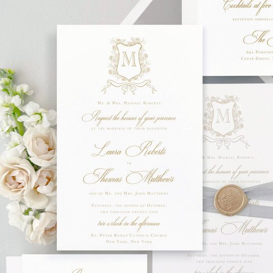 Classic wedding invitation featuring a Floral Monogram Crest with bow under it. Shown in gold ink features elegant script type. Optional embellishment shown is gray silk ribbon wrap finished with a gold wax seal. The envelope liner is gray velvet envelope liner. The name of this collection is Sofia. It is part of semi-custom wedding invitation collection.