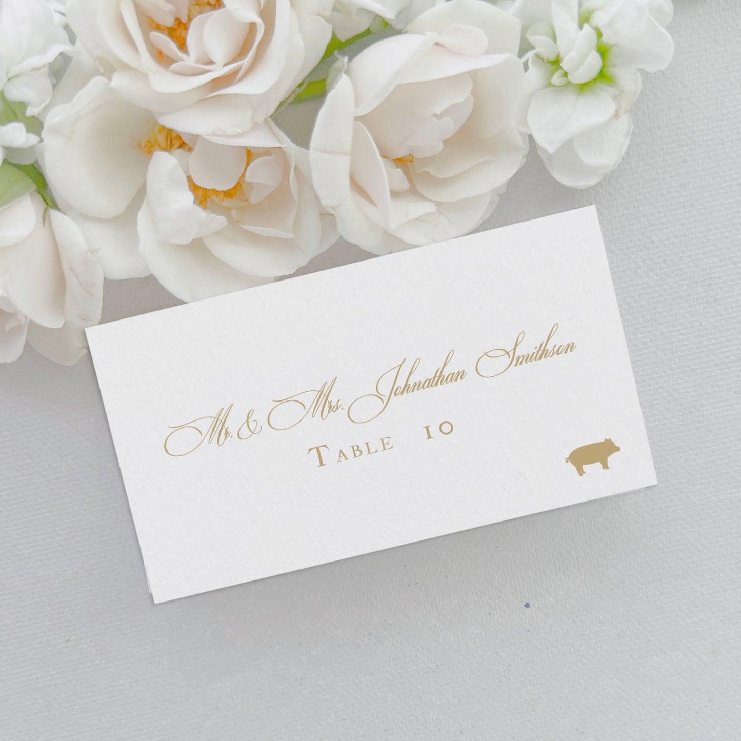 Flat wedding place card features gold ink, meal icon choice, script name, and text table number. They are 2x3.5 inches, the size of a business card. 