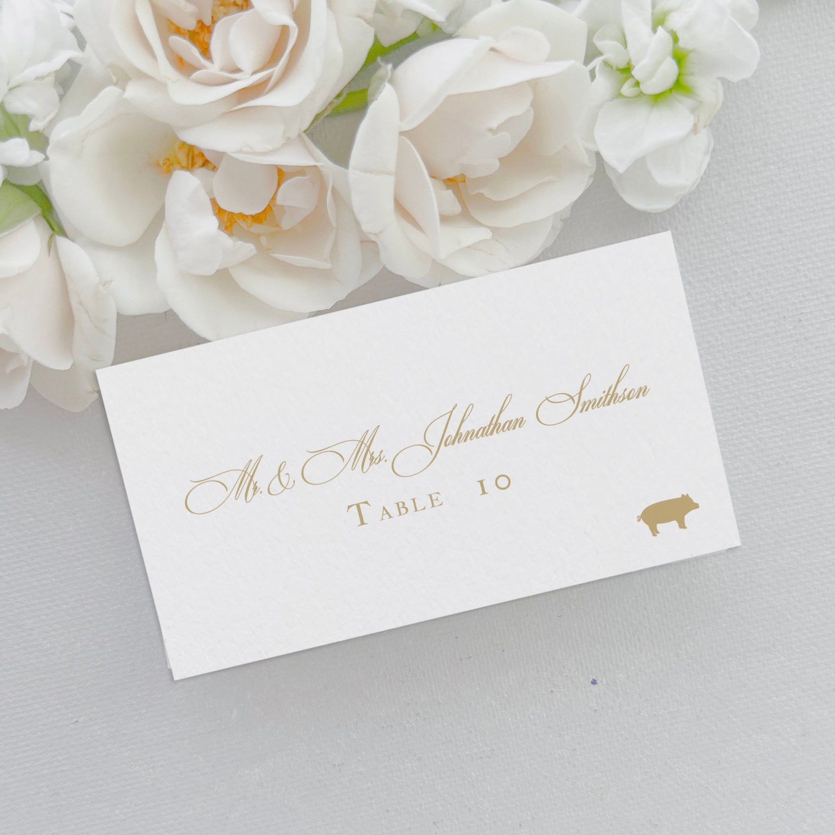 Flat wedding place card features gold ink, meal icon choice, script name, and text table number. They are 2x3.5 inches, the size of a business card. 